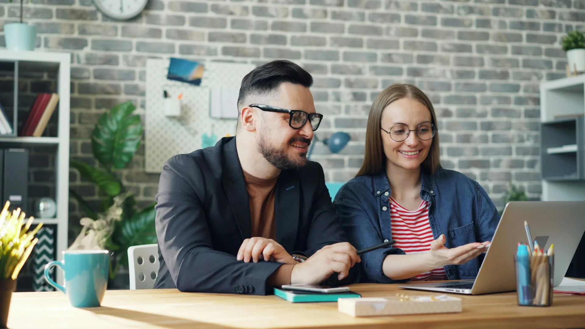 A man and a woman sitting at a table looking at a laptop together